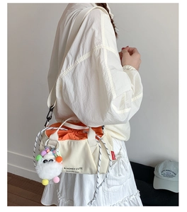 Detail of canvas bucket bag with orange drawstring and cute plush charm on shoulder strap
