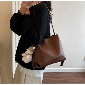 Brown leather bucket bag with plush dog charm worn by a model in a minimalist room