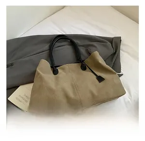 Dettaglio della borsa tote in tela kaki con manici neri su un letto con un blazer