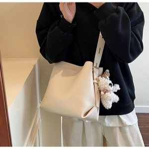 Minimalist cream bucket bag with cute plush bear charm on a matching wide shoulder strap