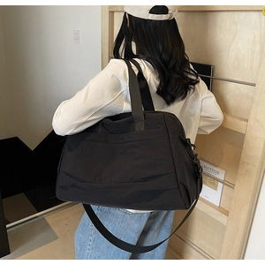 Vue détaillée d'un grand sac de voyage noir porté à l'épaule par un mannequin en studio