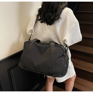 Detail view of large black nylon travel bag with adjustable strap on model back