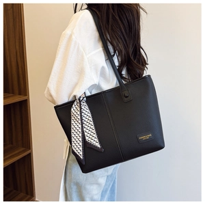 Close-up of black leather tote bag with silk scarf and logo plate on a model's shoulder