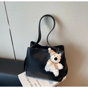 Detail of minimalist black leather tote bag with a cute plush bear charm on white books
