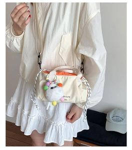 Detail of minimalist cream crossbody bag featuring orange lining and plush ball charm