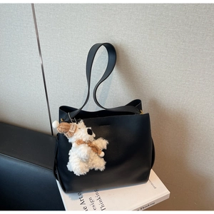 Detail of black matte leather tote bag featuring a cute plush polar bear charm on wide strap