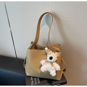 Close-up of khaki leather bucket bag with a cute plush bear charm and long shoulder strap