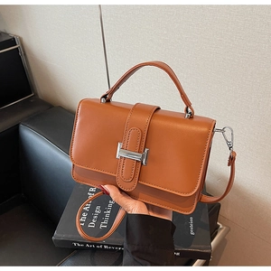 Detail view of brown faux leather handbag with silver metal buckle and adjustable strap