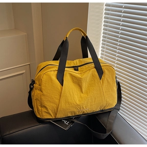 Detail of waterproof yellow nylon travel bag with black straps on a black leather sofa