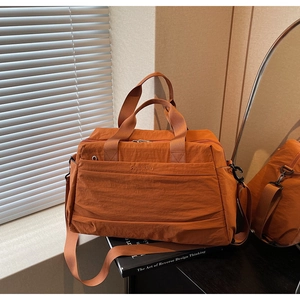 Détail du sac de voyage orange en nylon avec poignées et logo sur bois sombre