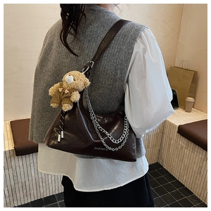 Detail der dunkelbraunen Glanztasche mit Metallketten und einem Teddybär-Anhänger