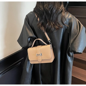 Detailed view of a beige crossbody bag featuring an H-shaped metal clasp on dark stairs