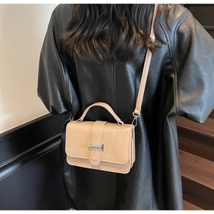 Detail of minimalist beige leather crossbody bag with silver buckle worn by a model