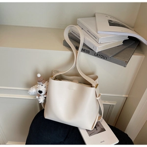 Detail of minimalist cream bucket bag with a cute puppy plush charm and adjustable strap