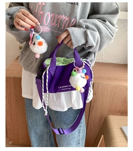 Detail view of purple drawstring crossbody bag with plush pom-poms and light green lining