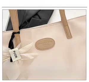 Close-up of beige tote bag with leather logo stamp and white floral charm detail