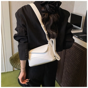 White lychee leather saddle bag with wide strap worn over a black blazer for chic style