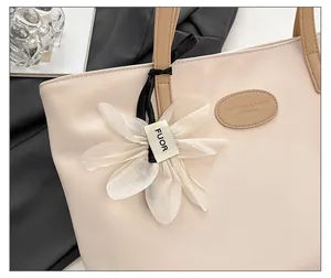 Detail of beige tote bag featuring a decorative white flower charm and embossed brand logo