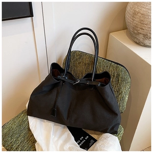 Dettaglio di una grande borsa da viaggio in tela nera con manici in pelle su sedia verde