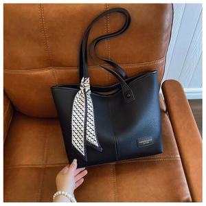 Detail of black pebbled leather tote bag with geometric silk scarf on brown sofa