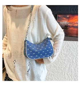 Blue denim underarm bag with white bow pattern and silver chain on model