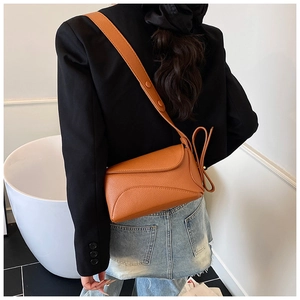 Detail of orange pebble leather crossbody bag with wide adjustable strap on black blazer