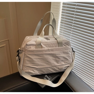 Gros plan du sac de voyage en toile beige avec larges poignées et bandoulière réglable