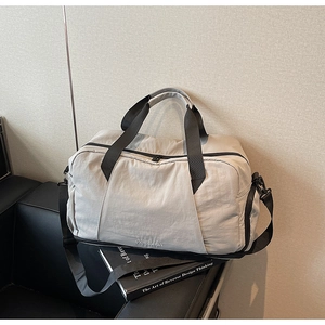 Detail view of a beige travel bag with black straps on a black leather sofa