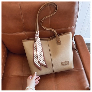 Detail of tan lychee grain leather tote bag with silk scarf and logo patch on sofa