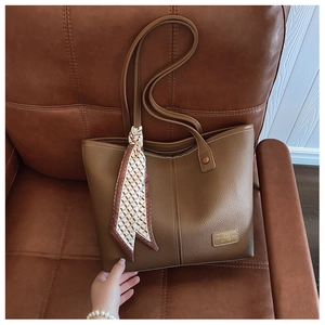 Close-up of brown lychee grain leather tote bag with elegant scarf and brand label