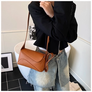 Brown litchi grain leather crossbody bag with curved flap shown on a model