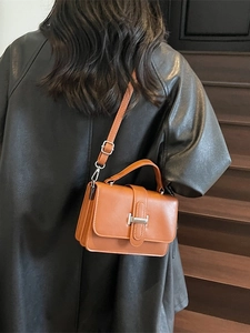 Chic brown faux leather handbag with H-shaped buckle on model in urban setting