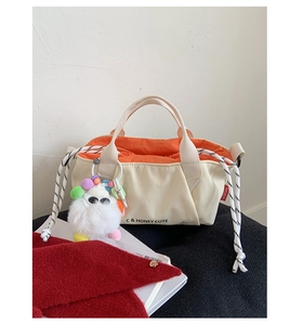 Detailed view of cream canvas drawstring bag with orange lining and cute plush monster charm