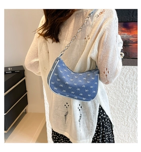 Detailed close-up of blue denim hobo bag with white bow pattern and silver chain strap