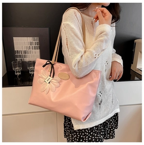 Detail of pink faux leather tote bag showing a white floral charm and bow decoration
