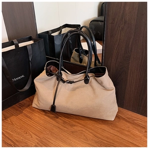 Dettaglio di una borsa da viaggio in tela kaki con manici in pelle nera e fibbia sottile