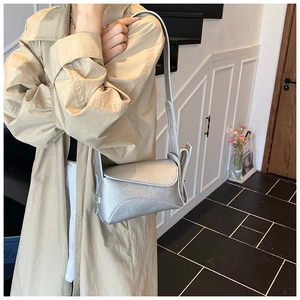 Silver textured crossbody bag with curved flap shown on model with khaki trench coat