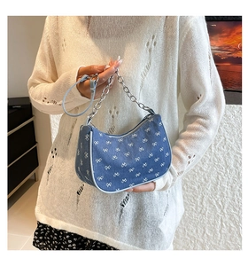 Detail of blue denim crescent bag featuring white bow prints and silver chain strap