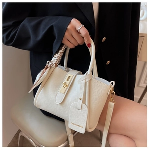 Détail du sac seau blanc avec cuir grainé, fermoir doré et anse ornée d'un foulard