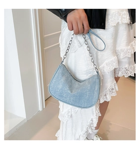 Detail view of light blue denim half moon bag with shimmering texture on a female model