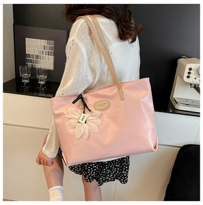 Pink faux leather tote bag with khaki strap and flower charm shown in a cozy indoor setting