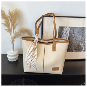 Chic cream tote bag with brown leather trim and silk scarf detail in a home setting