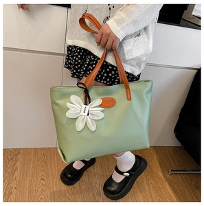 Detail of light green tote bag with brown leather handles and a white floral charm