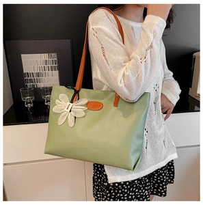 Light green large tote bag with orange handles and flower charm shown on shoulder
