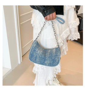 Close-up of blue denim crescent bag with silver chain strap worn by a model