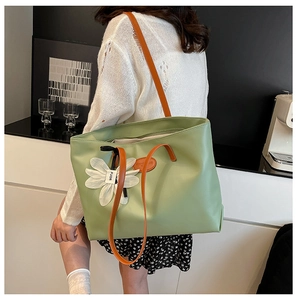 Detail of green leather tote bag with orange shoulder straps and white floral charm