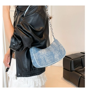 Detail of light blue denim crescent bag with silver chain worn by a stylish model