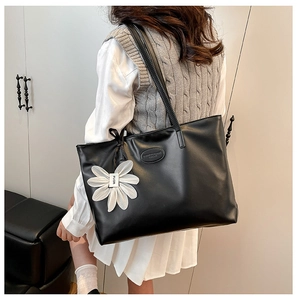 Detailed back view of a large black tote bag with a white flower charm accessory