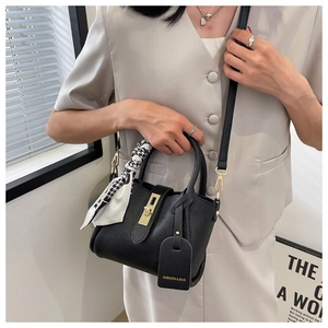 Détail d'un sac seau en cuir noir avec poignée en foulard pied-de-poule et boucle dorée