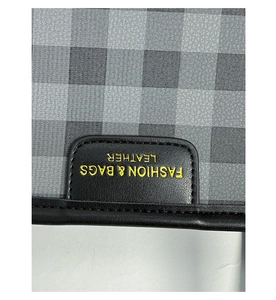 Detail of checkered fabric tote with gold embossed fashion lettering on black leather